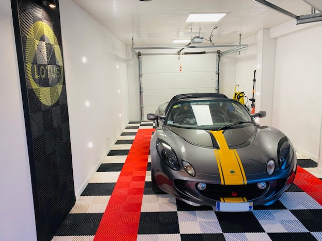 Logo Lotus sur dalles SquareFLOOR noir au mur d'un garage avec une Lotus